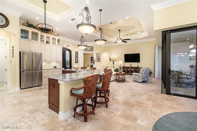 kitchen featuring a tray ceiling, pendant lighting, stainless steel fridge, and a large island with sink