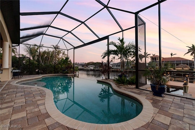 pool at dusk featuring a patio area, a lanai, and a water view