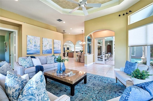 living room featuring light tile patterned floors, ceiling fan with notable chandelier, a raised ceiling, and crown molding