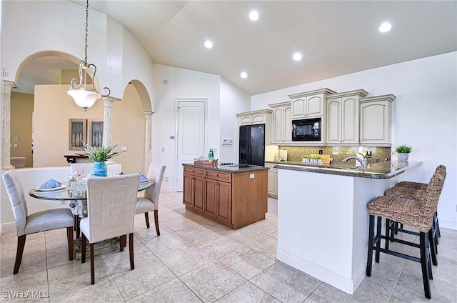 kitchen with backsplash, dark stone counters, black appliances, kitchen peninsula, and decorative columns