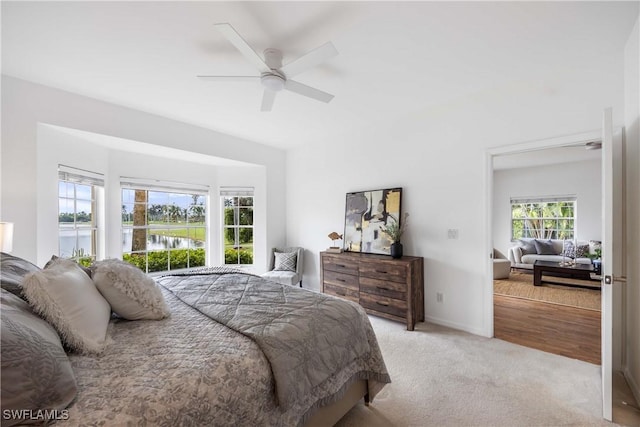 carpeted bedroom featuring multiple windows, ceiling fan, and a water view