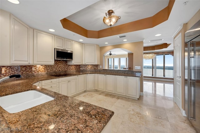 kitchen featuring sink, stainless steel appliances, a water view, kitchen peninsula, and a raised ceiling