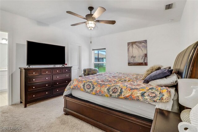 bedroom with ceiling fan, light colored carpet, and ensuite bath