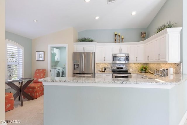 kitchen with stainless steel appliances, kitchen peninsula, lofted ceiling, white cabinets, and washer and dryer