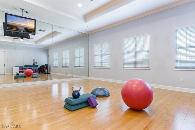 exercise room with a tray ceiling, crown molding, baseboards, and wood finished floors