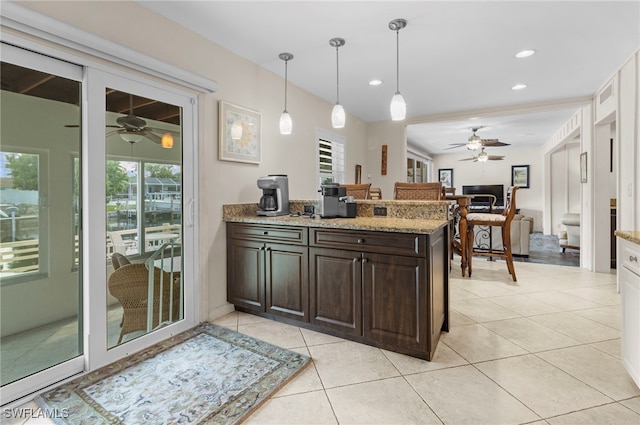 kitchen with hanging light fixtures, dark brown cabinetry, light tile patterned floors, light stone counters, and kitchen peninsula