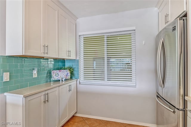 kitchen featuring decorative backsplash, light tile patterned floors, white cabinetry, and stainless steel refrigerator