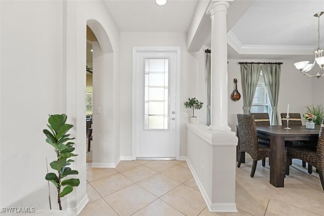 entrance foyer with ornate columns, light tile patterned floors, crown molding, and an inviting chandelier