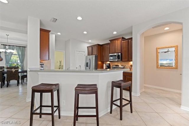 kitchen with backsplash, hanging light fixtures, light tile patterned floors, a kitchen bar, and stainless steel appliances