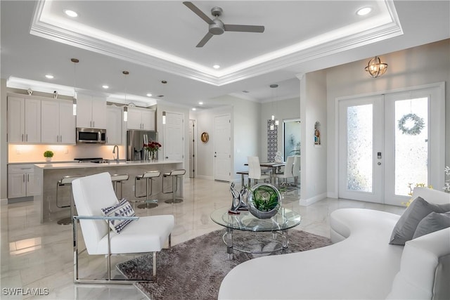 living room with french doors, sink, crown molding, a tray ceiling, and ceiling fan with notable chandelier