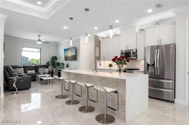 kitchen featuring pendant lighting, white cabinets, a center island with sink, ornamental molding, and appliances with stainless steel finishes