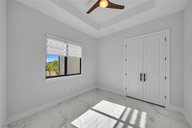 unfurnished bedroom featuring a raised ceiling, ceiling fan, and a closet