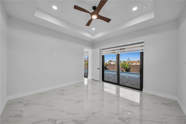 empty room with ceiling fan and a tray ceiling