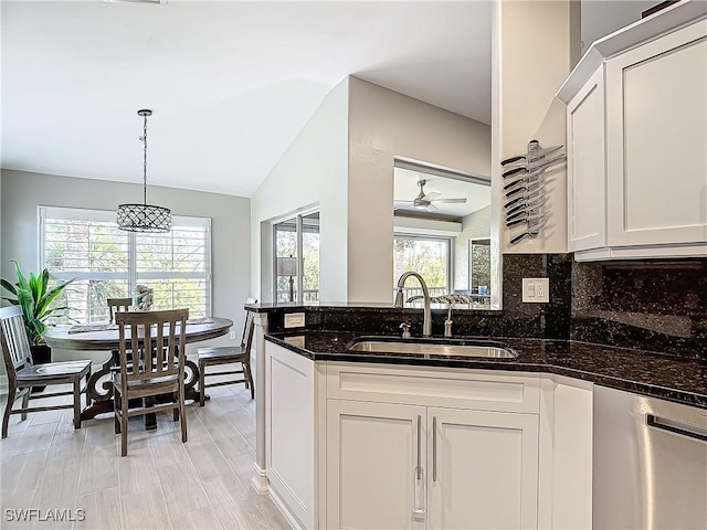 kitchen with stainless steel dishwasher, white cabinetry, sink, and dark stone counters