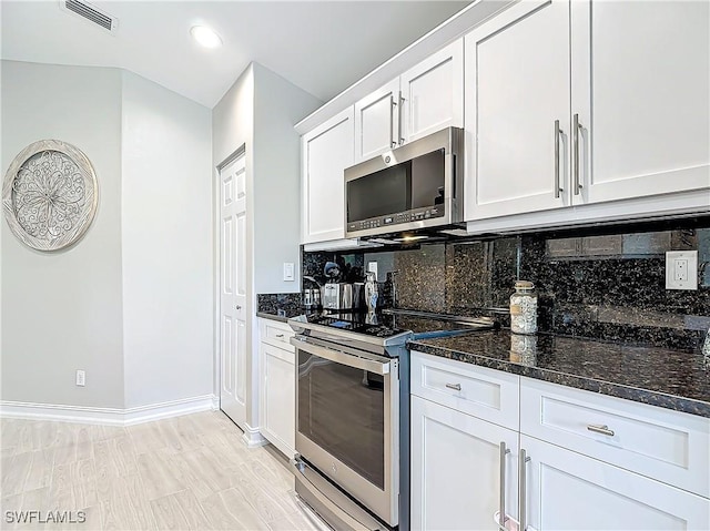 kitchen featuring white cabinets, light hardwood / wood-style flooring, dark stone countertops, appliances with stainless steel finishes, and tasteful backsplash