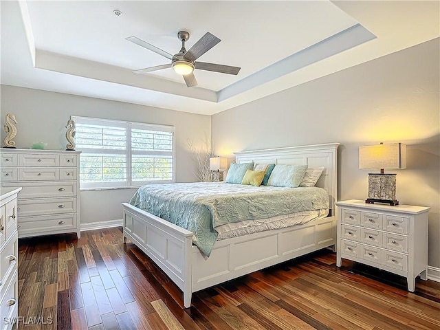 bedroom with dark hardwood / wood-style floors, ceiling fan, and a tray ceiling