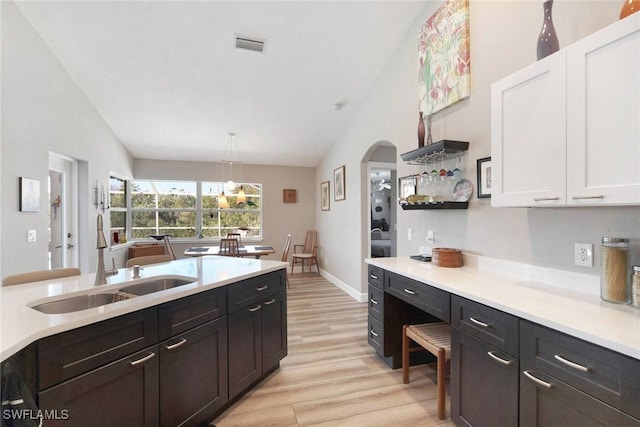 kitchen featuring sink, pendant lighting, vaulted ceiling, white cabinets, and light wood-type flooring