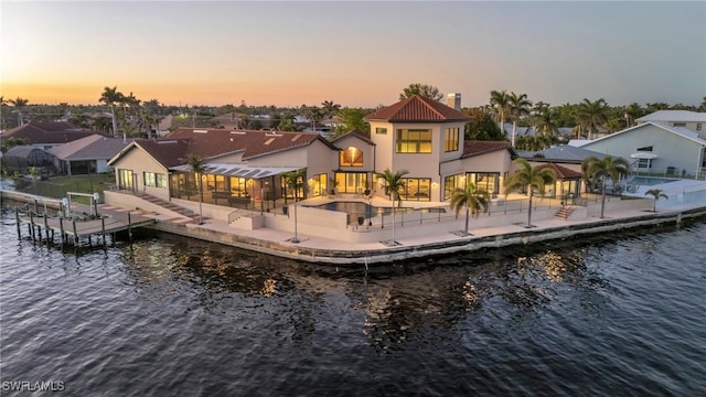 back house at dusk with a water view, a pool, a patio area, and a sunroom