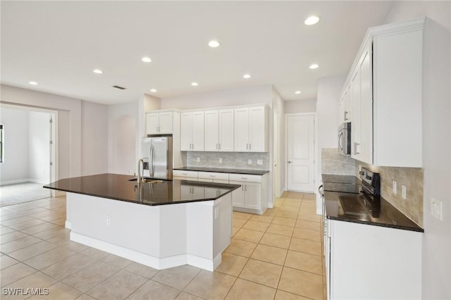 kitchen with light tile patterned flooring, appliances with stainless steel finishes, white cabinetry, sink, and a center island with sink