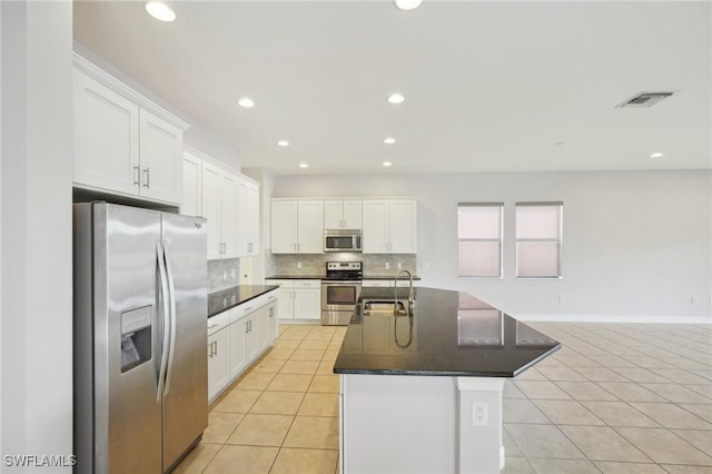 kitchen with appliances with stainless steel finishes, an island with sink, sink, white cabinets, and light tile patterned floors