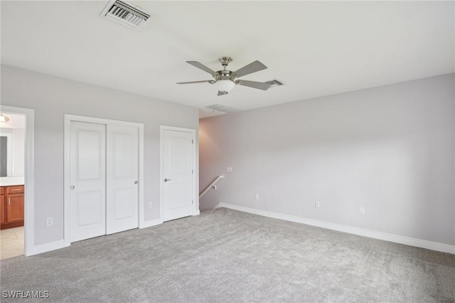 unfurnished bedroom featuring ceiling fan, light colored carpet, multiple closets, and ensuite bath