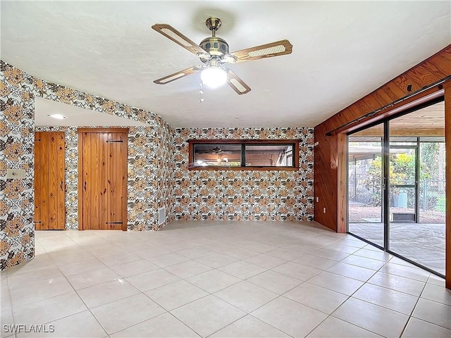 unfurnished room featuring ceiling fan, wood walls, and light tile patterned floors