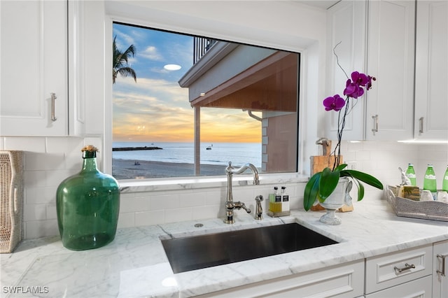 kitchen featuring white cabinetry, tasteful backsplash, light stone countertops, a water view, and sink