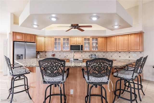 kitchen featuring appliances with stainless steel finishes, a breakfast bar, light stone counters, and decorative backsplash