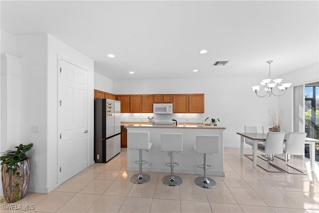 kitchen with stainless steel refrigerator, an inviting chandelier, decorative light fixtures, a kitchen bar, and a kitchen island with sink