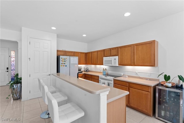 kitchen featuring a breakfast bar, white appliances, beverage cooler, light tile patterned floors, and a kitchen island