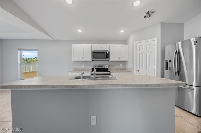 kitchen with appliances with stainless steel finishes, sink, light tile patterned floors, a center island with sink, and white cabinetry