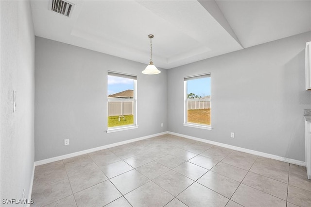 empty room featuring light tile patterned floors, a wealth of natural light, and a tray ceiling