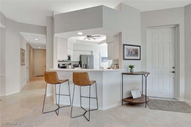 kitchen with white cabinets, ceiling fan, appliances with stainless steel finishes, kitchen peninsula, and a breakfast bar area