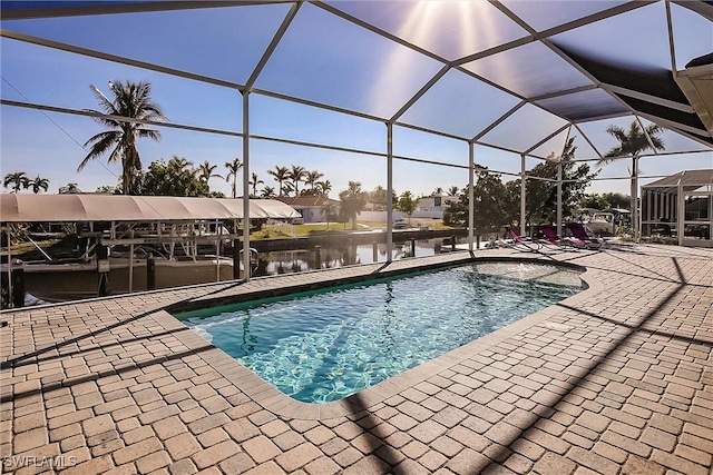 view of pool featuring glass enclosure, a water view, and a patio