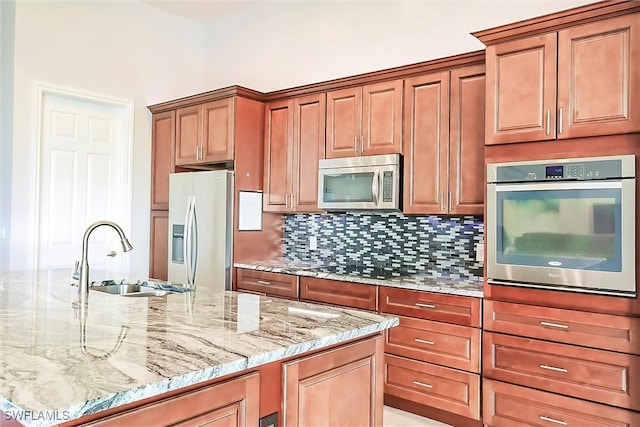 kitchen featuring stainless steel appliances, light stone counters, tasteful backsplash, and sink