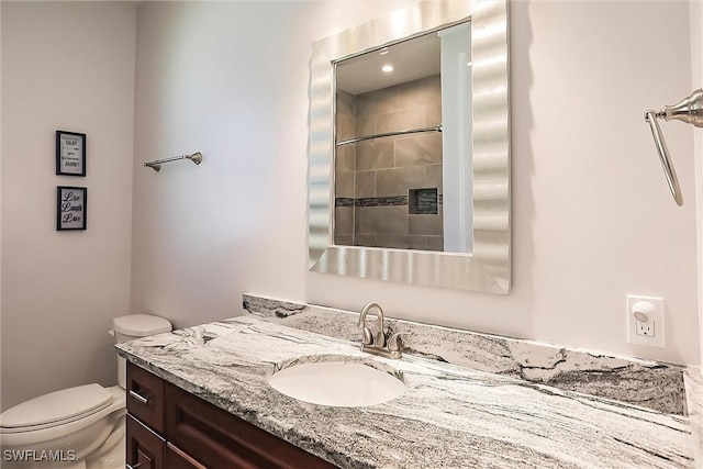 bathroom featuring a tile shower, vanity, and toilet