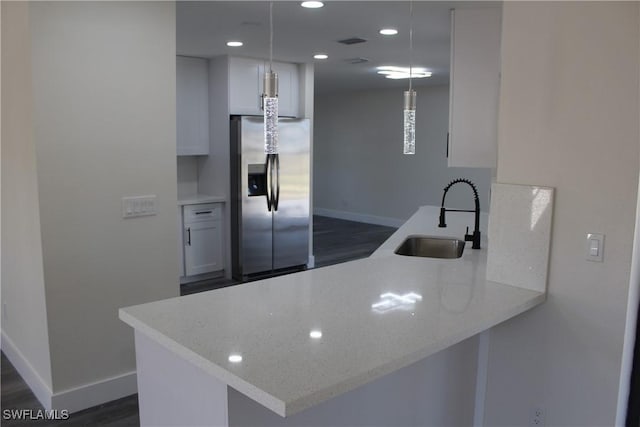 kitchen with kitchen peninsula, sink, stainless steel fridge with ice dispenser, white cabinetry, and hanging light fixtures