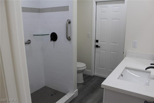 bathroom featuring tiled shower, vanity, hardwood / wood-style flooring, and toilet