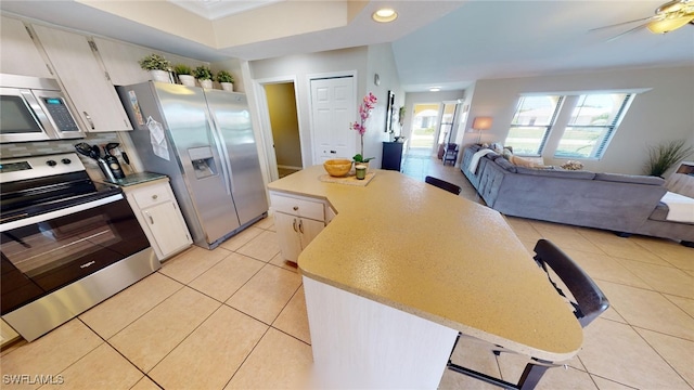 kitchen with appliances with stainless steel finishes, ceiling fan, light tile patterned floors, a center island, and white cabinetry