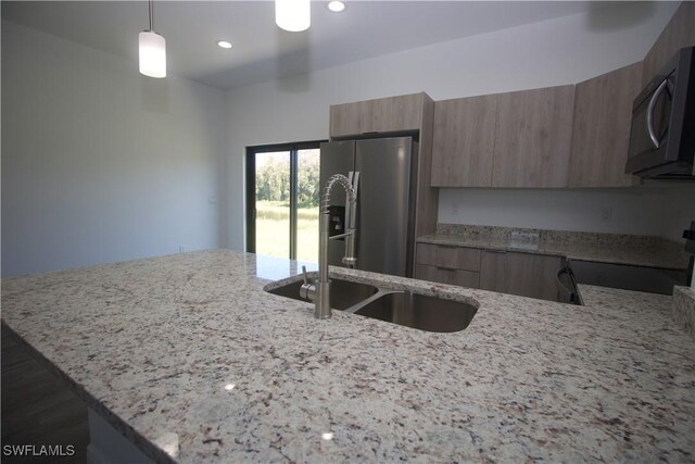 kitchen featuring light stone countertops, stainless steel fridge, stove, sink, and decorative light fixtures