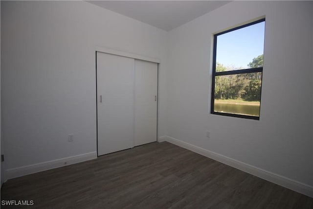 unfurnished bedroom with dark hardwood / wood-style floors, a closet, and multiple windows