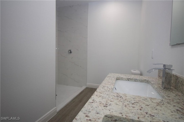 bathroom with tiled shower, wood-type flooring, vanity, and toilet