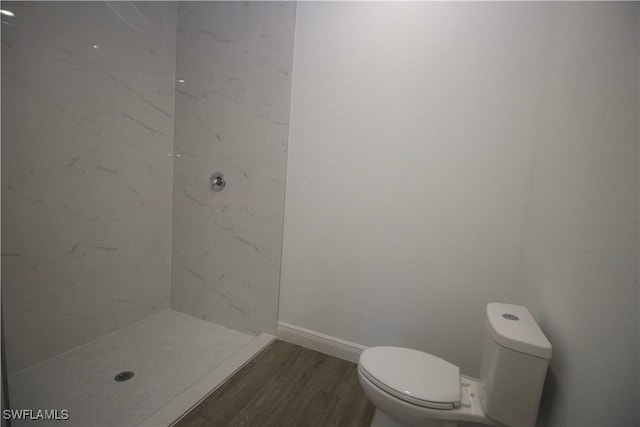 bathroom featuring hardwood / wood-style flooring, toilet, and tiled shower