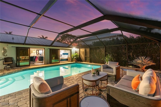 pool at dusk with an outdoor living space, a patio area, and a lanai