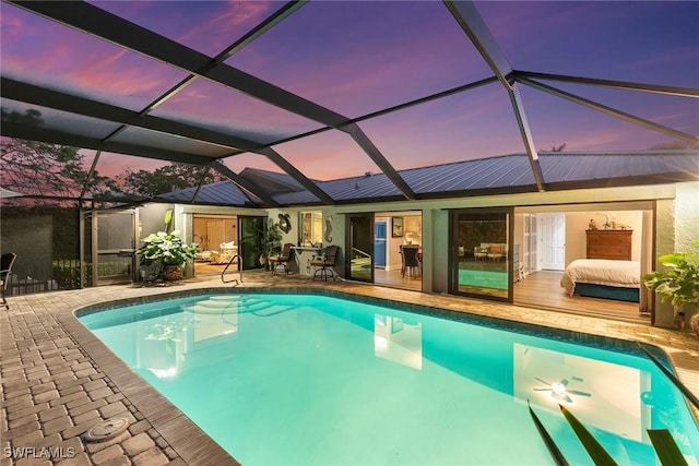 pool at dusk with glass enclosure and a patio