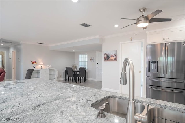 kitchen with white cabinets, ceiling fan, stainless steel fridge, ornamental molding, and light stone counters