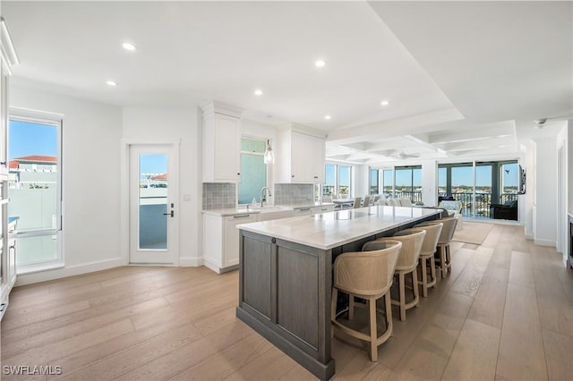 kitchen with a breakfast bar, sink, white cabinets, a center island, and light hardwood / wood-style floors