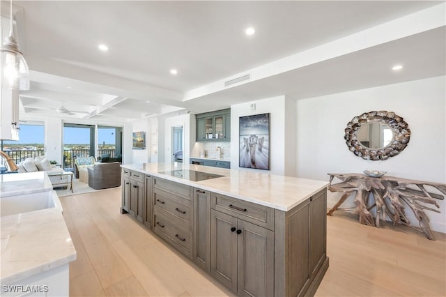 kitchen featuring light wood-type flooring, light stone counters, ceiling fan, sink, and beam ceiling