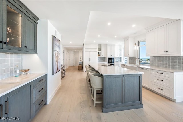 kitchen with white cabinets, light wood-type flooring, backsplash, and a large island