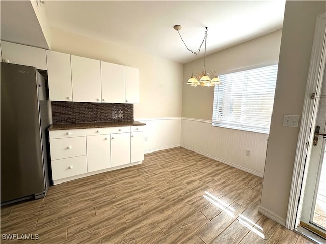 kitchen featuring stainless steel refrigerator, white cabinets, light hardwood / wood-style floors, and a notable chandelier